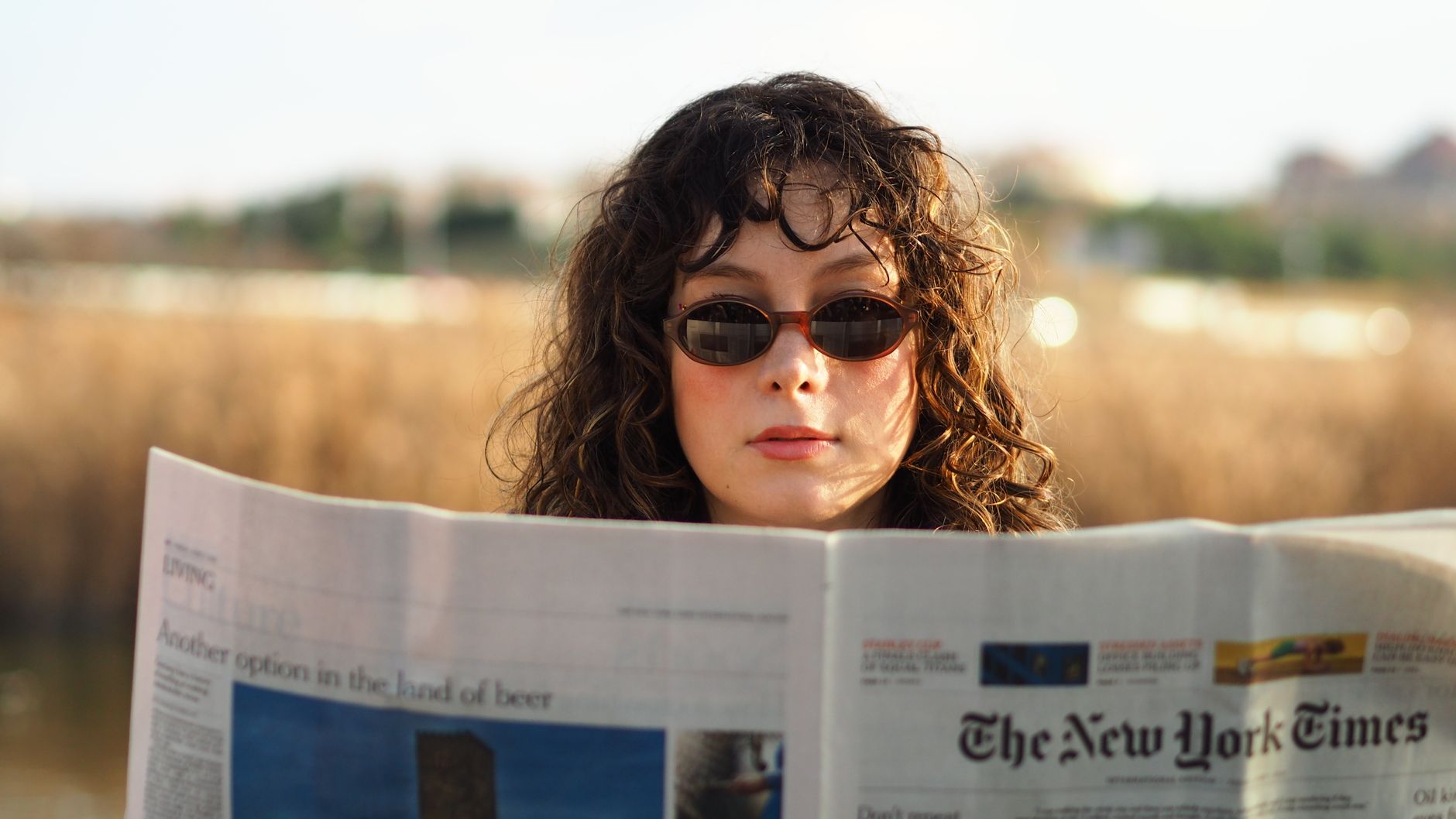 Young woman wearing sunglasses reading a newspaper in a natural outdoor setting. — Unveiling the Magic of Botox Injections at